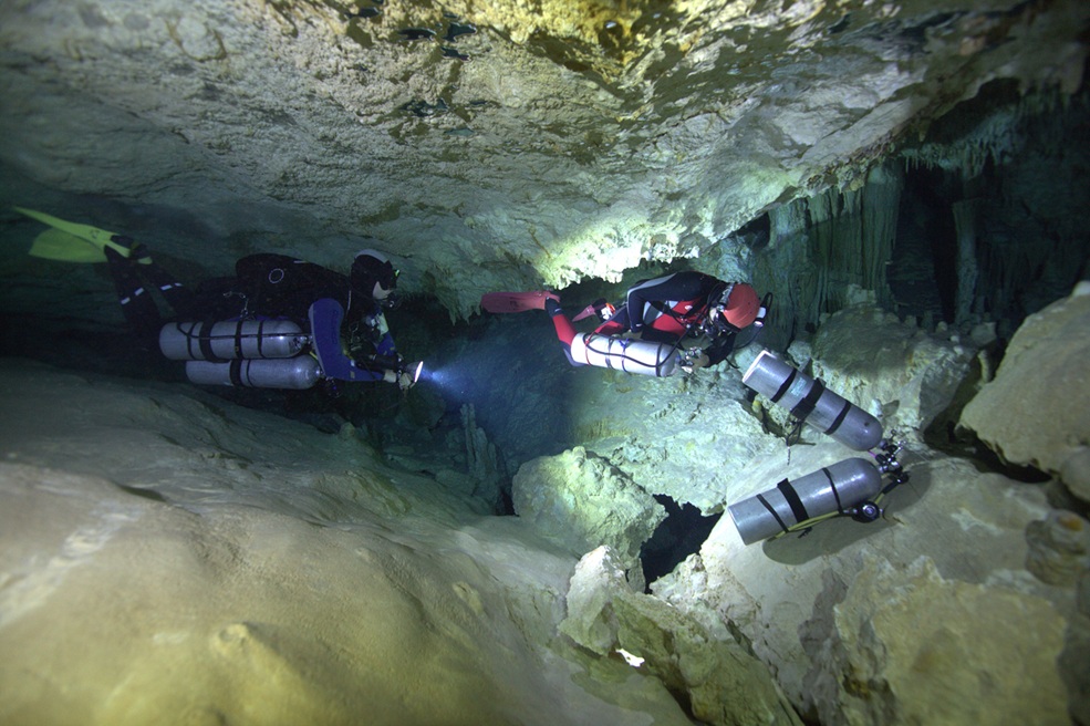 Cave divers removing their tanks before passing a major restriction